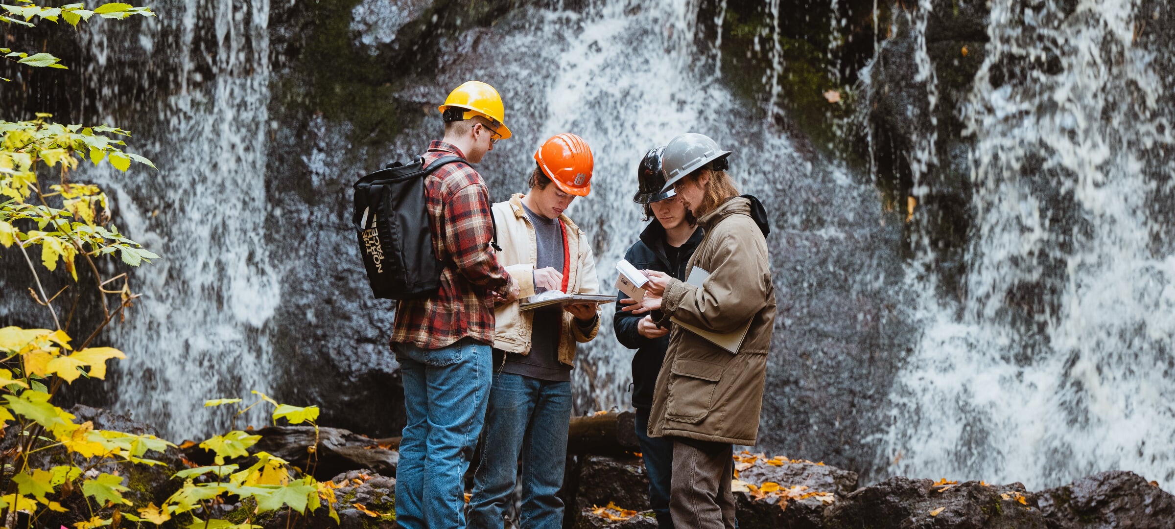 Students with hard hats in front of a rocky waterfall