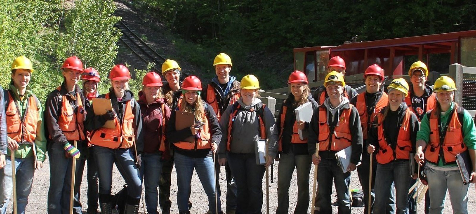 Students with hard hats and orange vests standing in front of the tram at the mine.