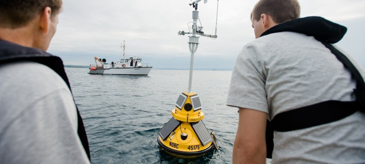 Two researchers deploying a buoy in the water.