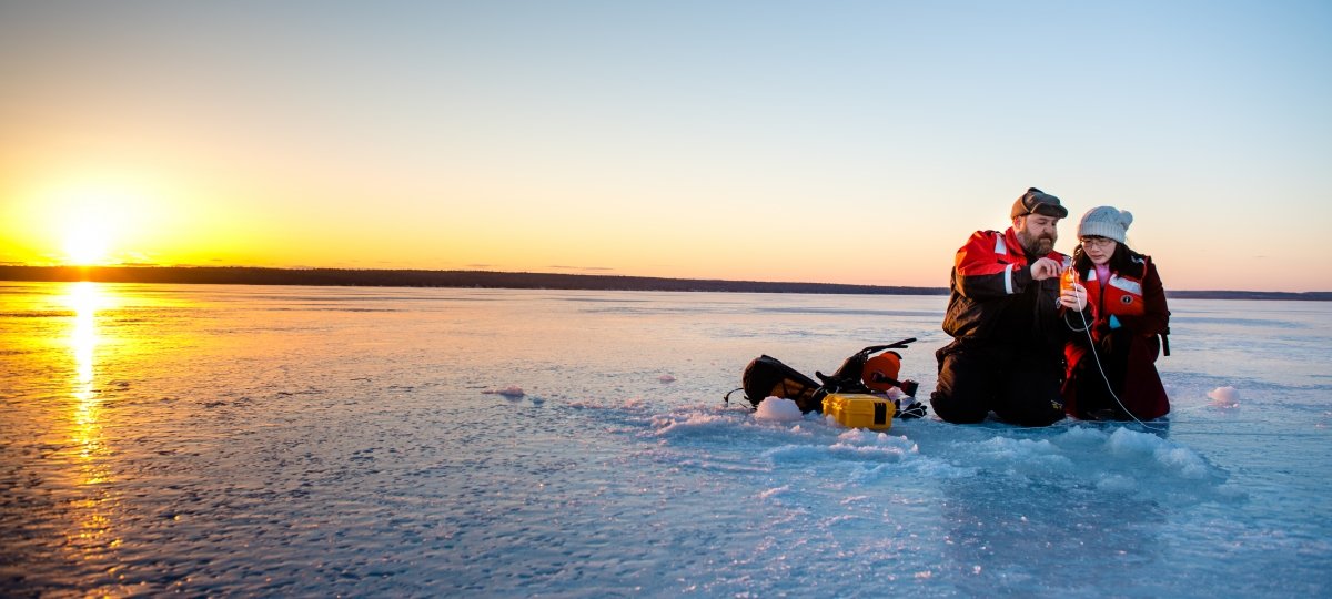 Two researchers kneeling on the ice reviewing data.