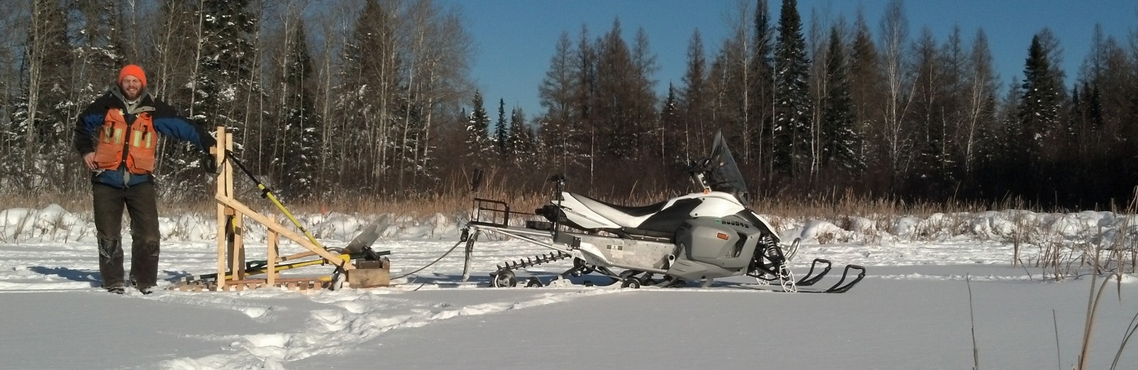 David Szyszkoski standing in the snow with a snowmobile hooked up to a sled.