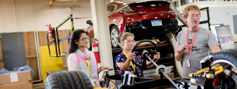 Two women and a man work on a car in a lab.