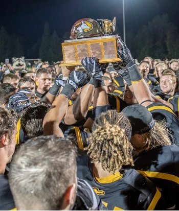 The Michigan Tech football team hoists a trophy into the air.