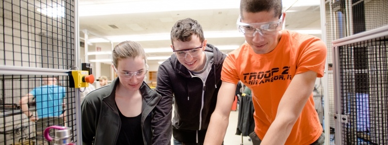 Three students wearing safety goggles review data on a computer.