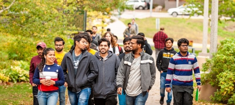 A group of students walks on the campus mall in early fall.