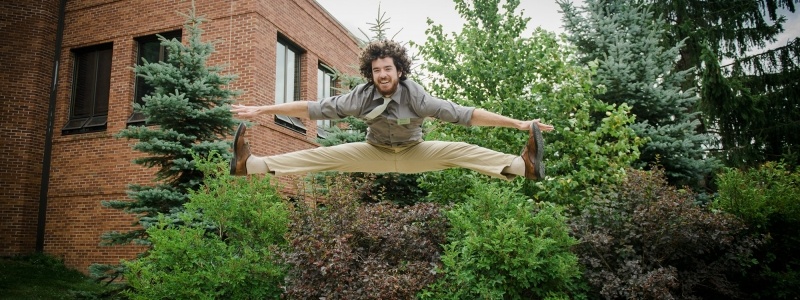 A student in a dress shirt and tie does a jumping split in front of the Memorial Union Building.