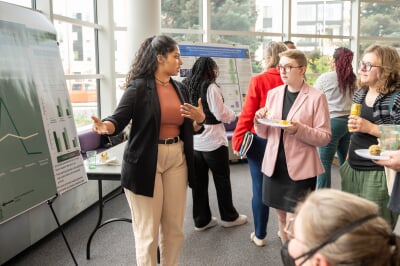 A student presents a research poster to a small crowd at an event.