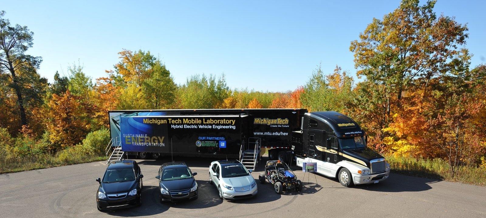 The mobile APS Labs surrounded by two trucks and one car.