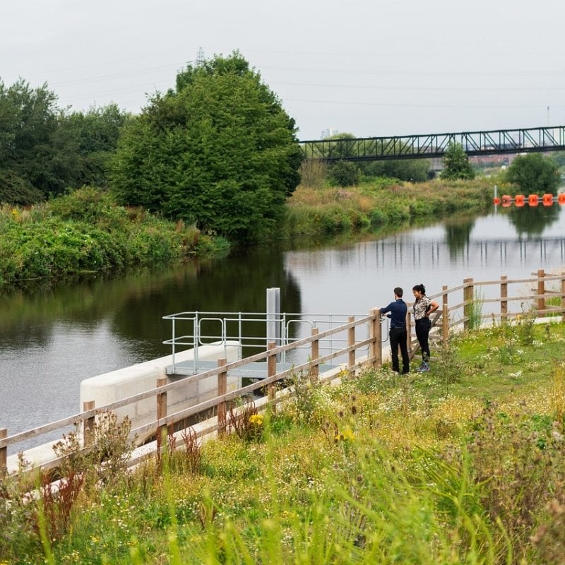 Two civil engineers discussing a plan near a riverbank.