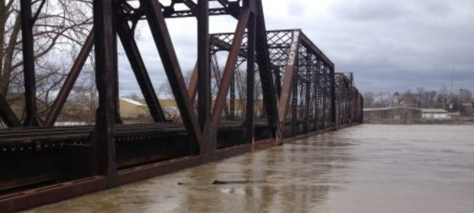 A flooded railroad bridge surrounded by muddy water.