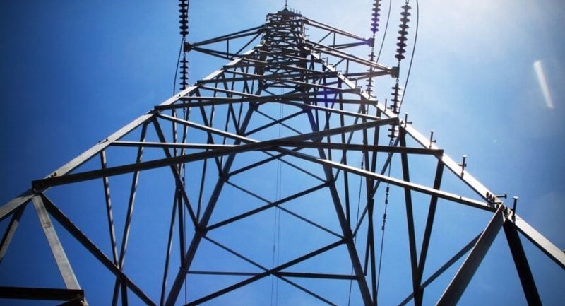 Looking up from the bottom of an electric power tower against the backdrop of a deep blue sky.