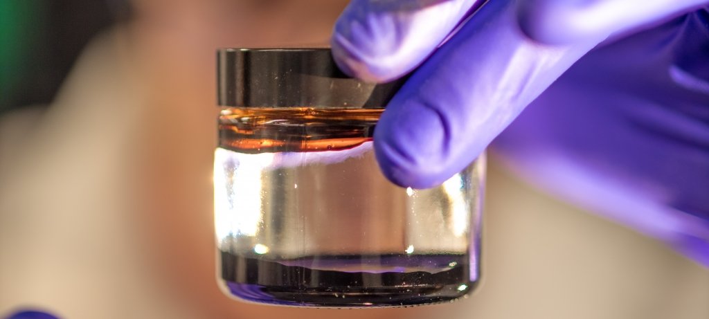 Researcher hold a container of liquid with gloves.