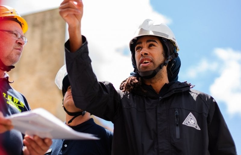 A GIS expert on the site of a disaster, pointing upwards while talking.