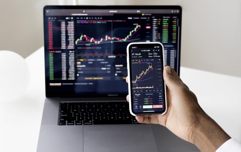 A person looking at data on their smartphone, which is held in front of a computer screen.