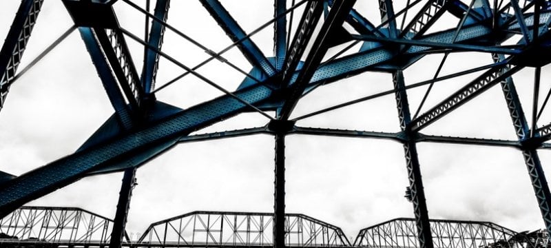 Close up of steel beams of a bridge, with another bridge in the background.