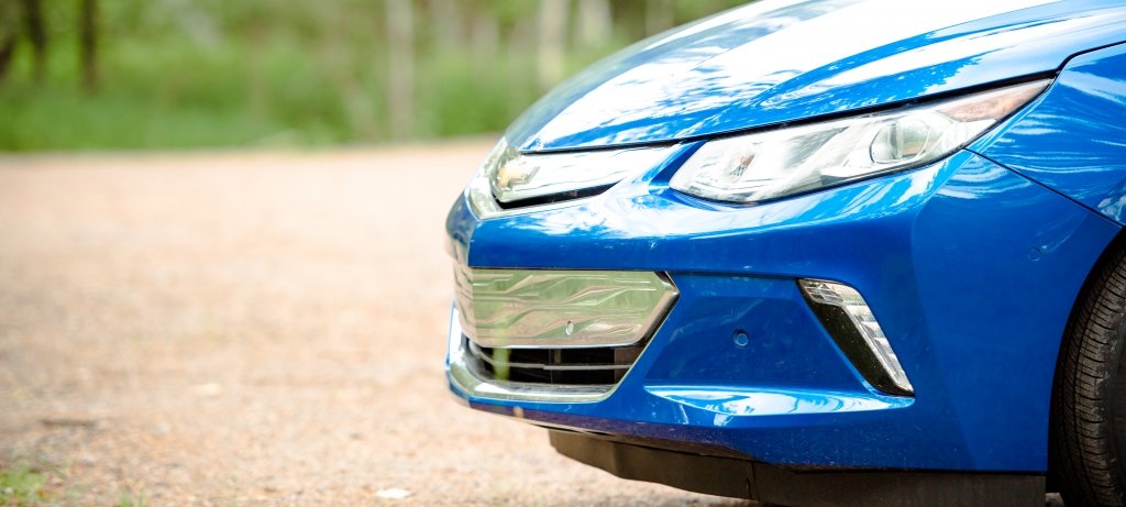 Front section of a parked car on a dirt road in the woods.