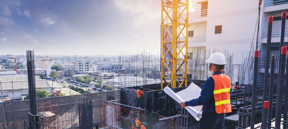 A civil engineer standing on the top of a building. They have a plan in their hand.