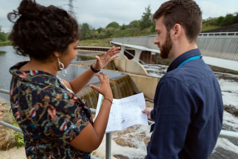 Two water engineers talk in front of a dam.