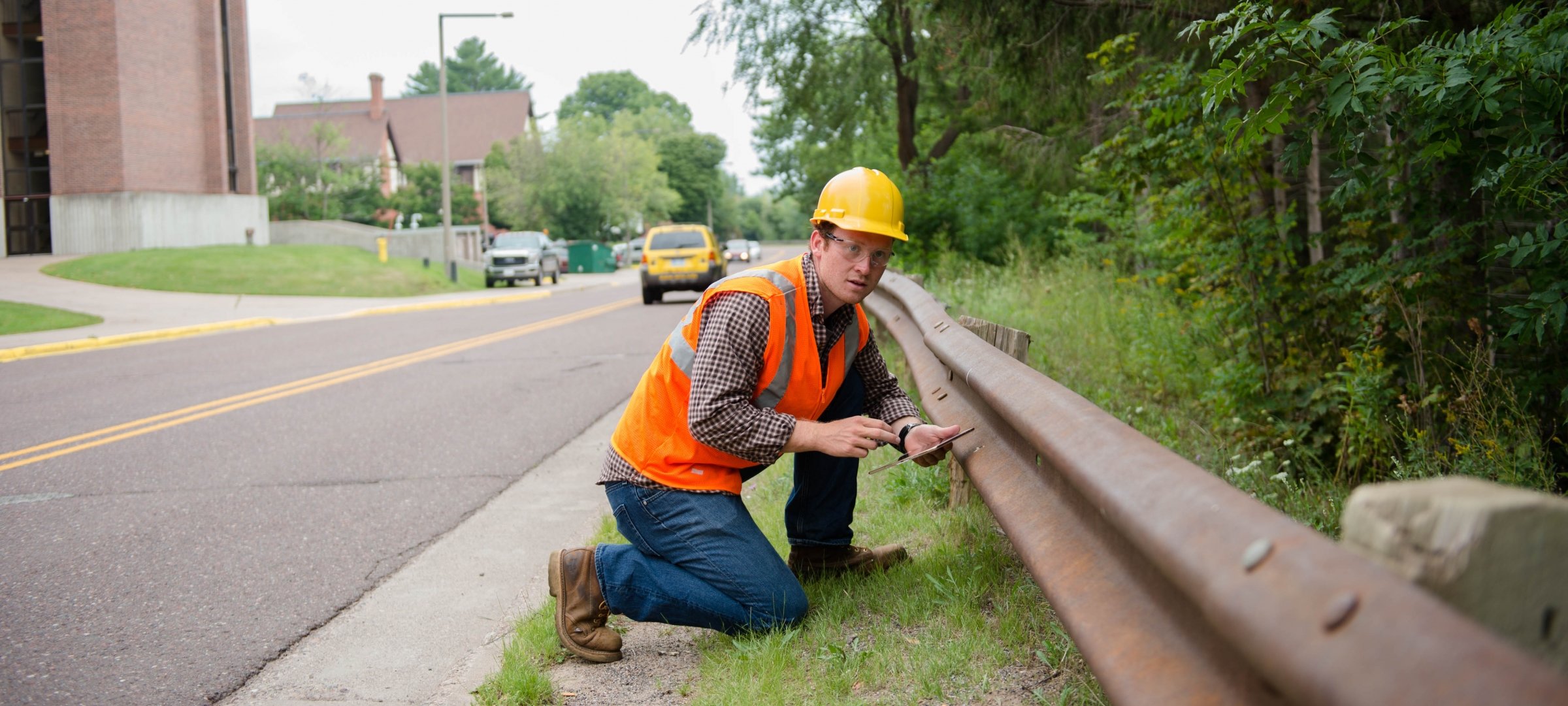 Civil engineering student in a hard hat, who is next to a guardrail on a city street.