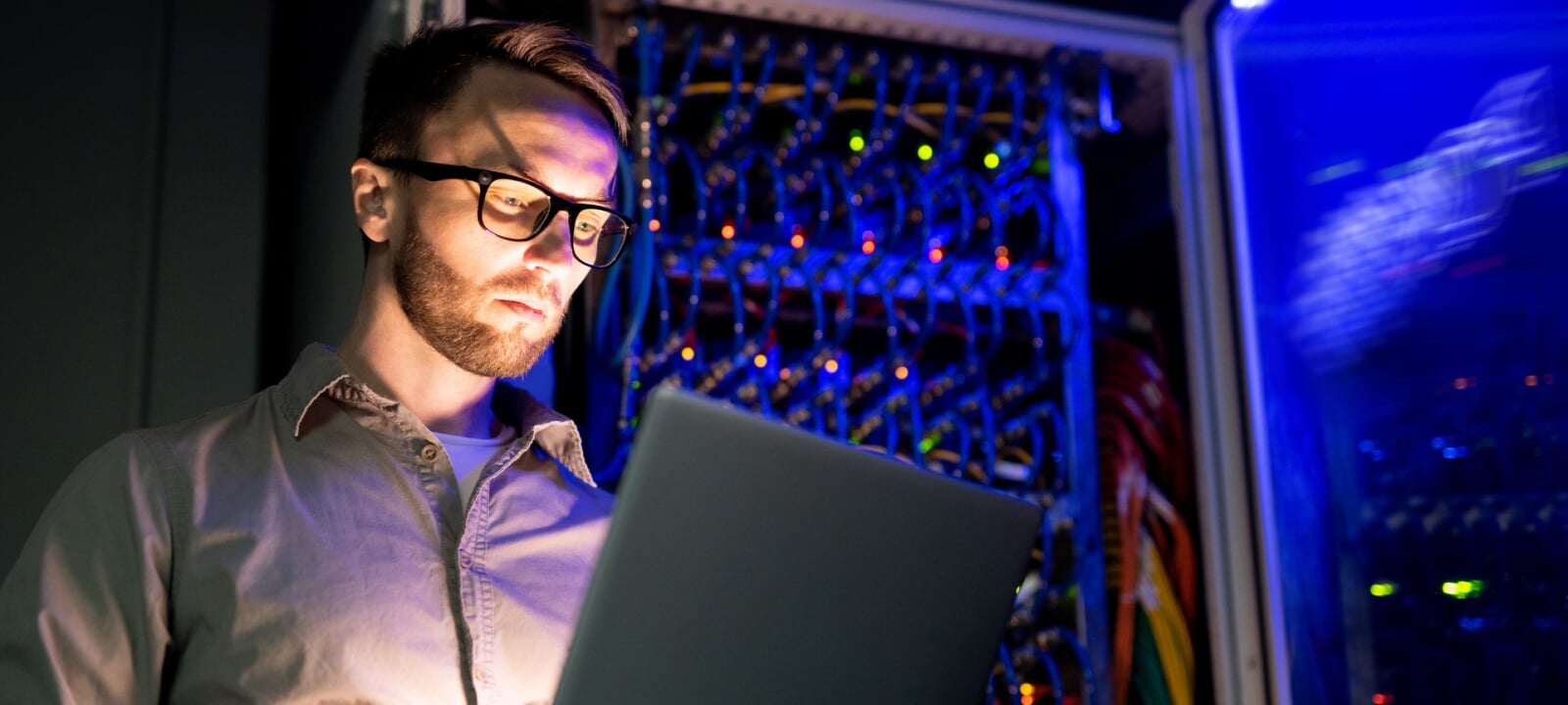 Your computer engineer looking at a laptop while standing in front of a large, open mainframe computer.