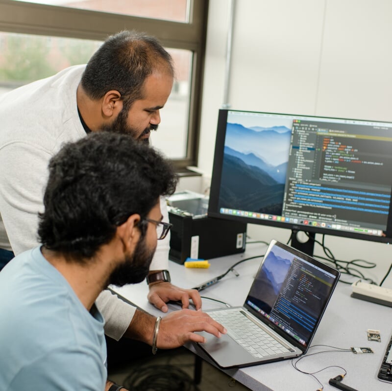Two men look at a computer trying to solve a cybersecurity problem.