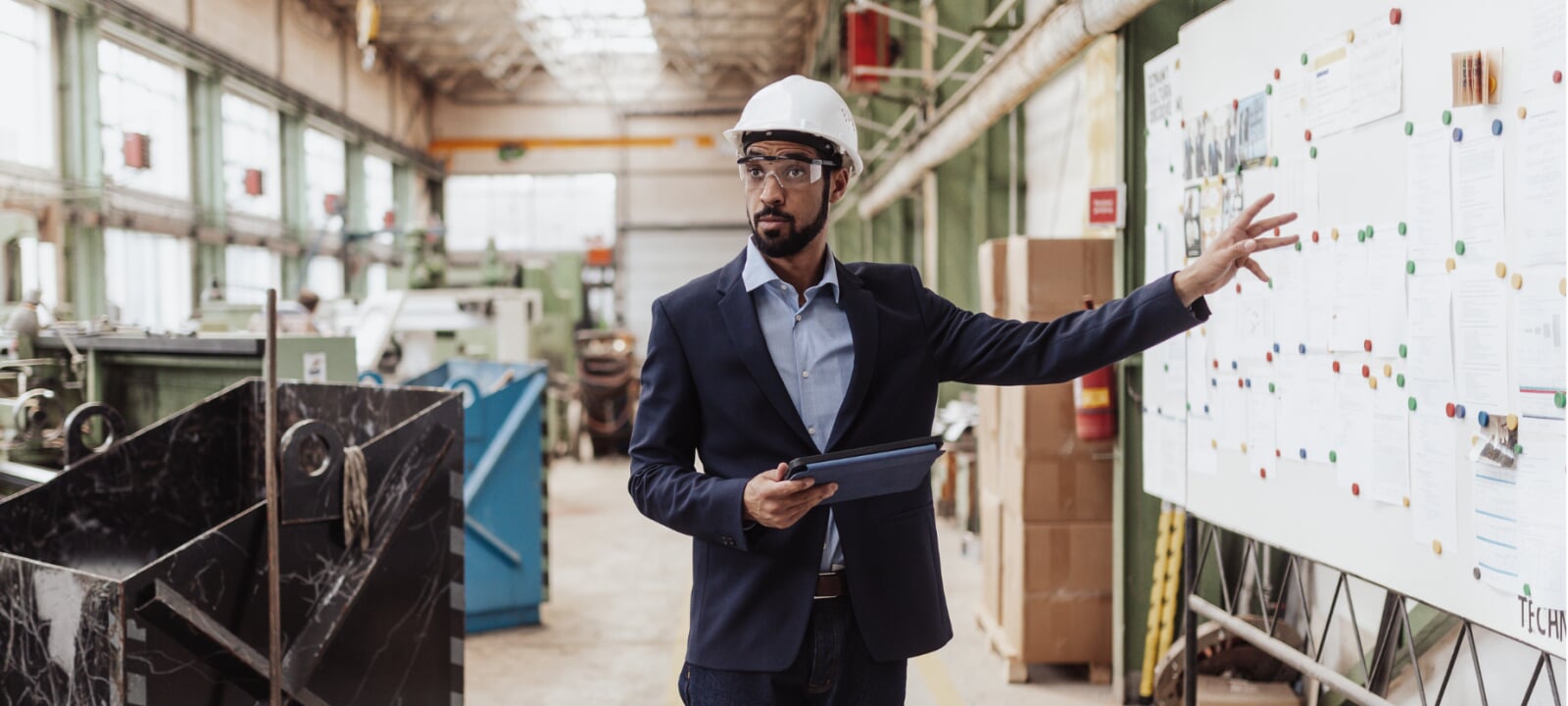 Engineering manager making a presentation and pointing to a white board while he is in a factory location.