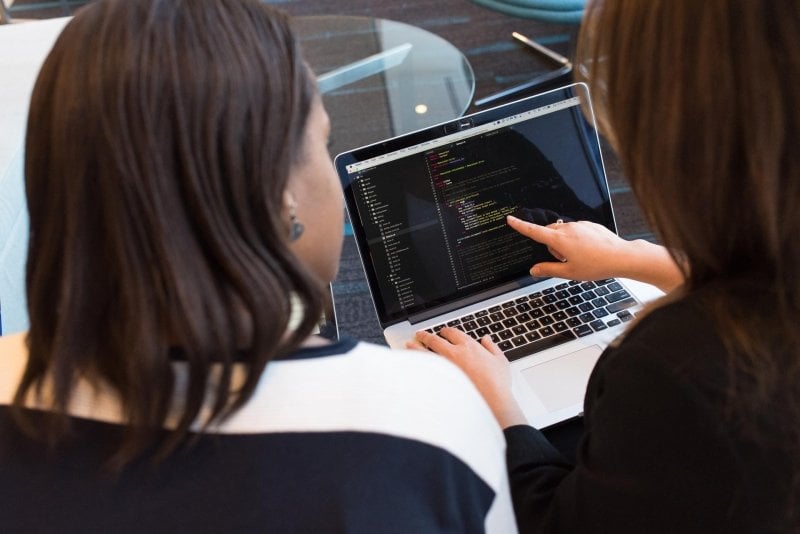 Two women looking at code on laptop.