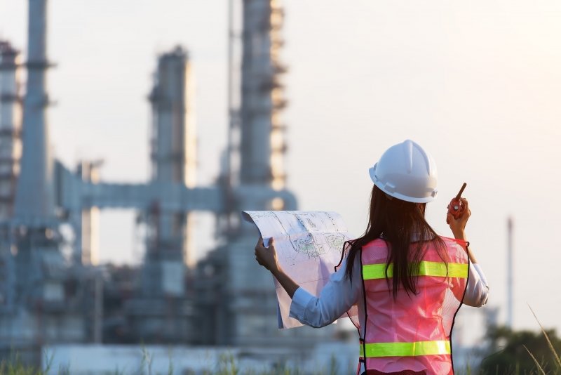 A female engineer standing in front a power plant, which is in the background.