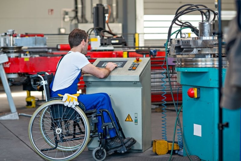 An engineer in a wheelchair checks on a machine in an industrial setting.