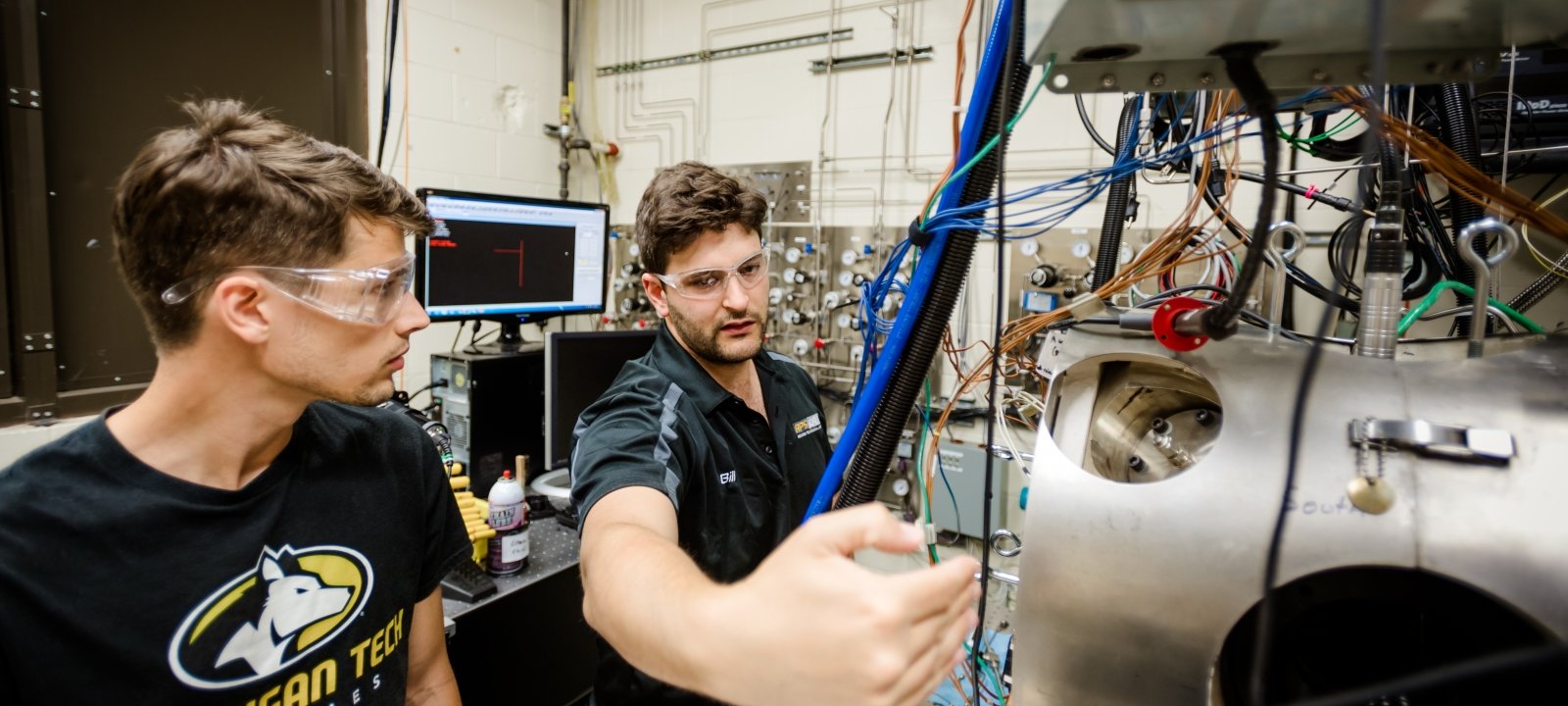 Two mechanical engineering students in a lab working on a piece of motorized equipment.