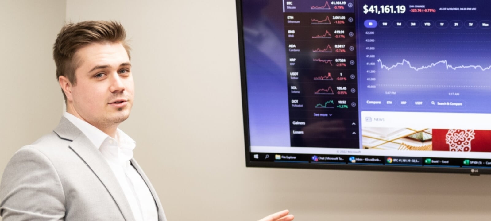 Business administration guy standing in front of a monitor while making a presentation about stocks.