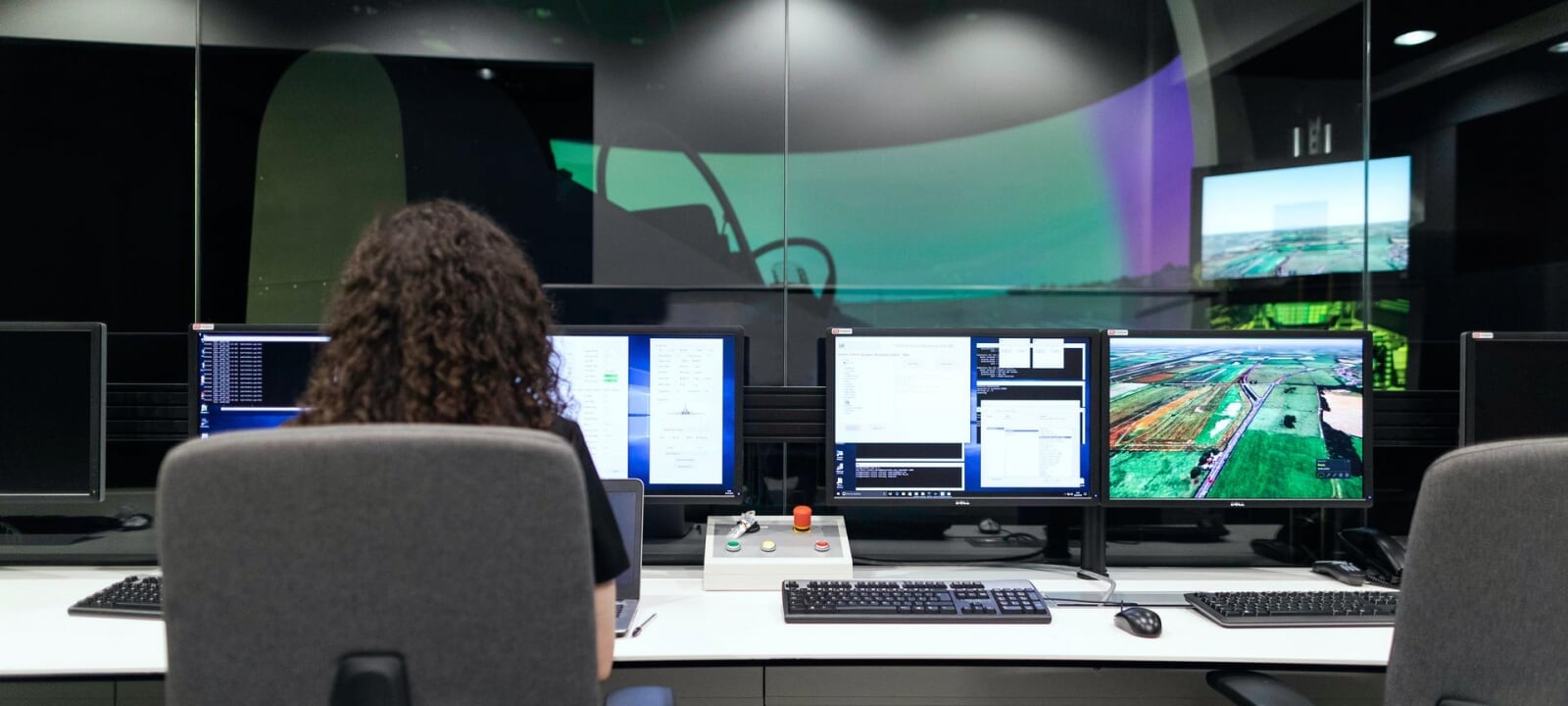 Female geospatial engineer looking at several computer monitors with images of maps and data while in a workplace setting.