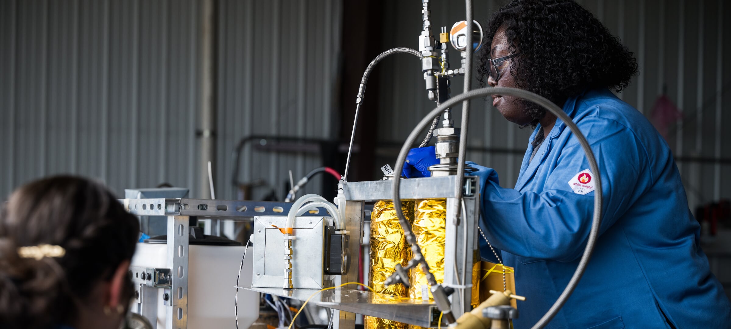 Two students in lab safety gear work on a pyrolysis machine demo.