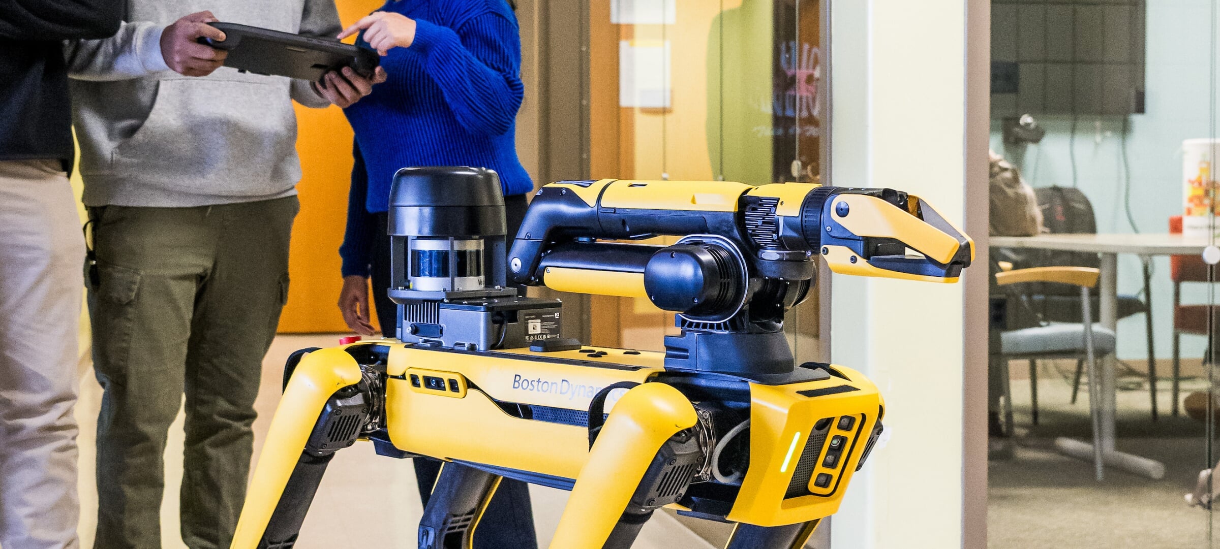 The body and head of a yellow "dog" robot, with students in the background controlling it.
