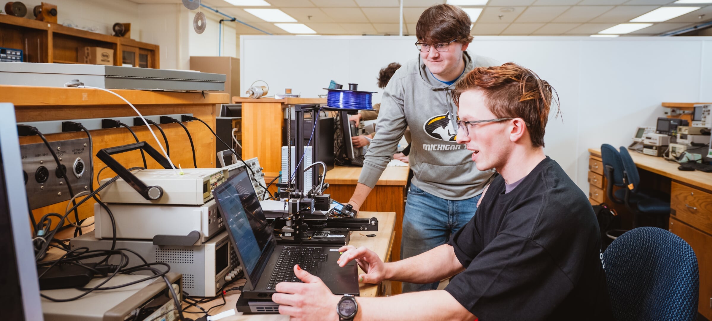 Two students review a laptop hooked up to an array of equipment.