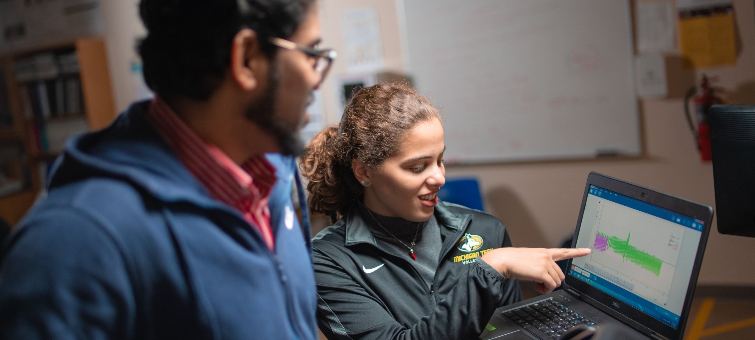 Grad student standing holding a laptop pointing with another student