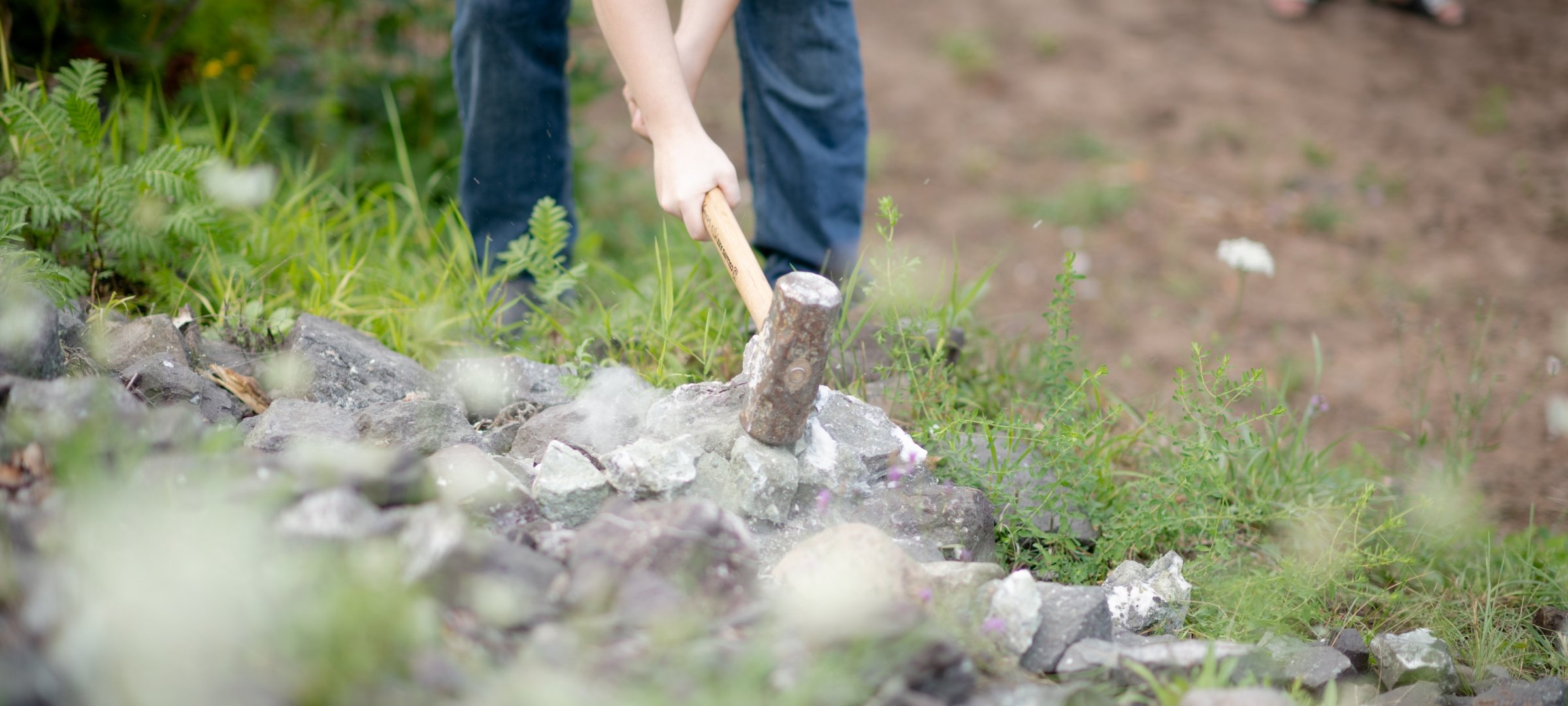 Researcher with a large hammer breaking rock in a remote area.
