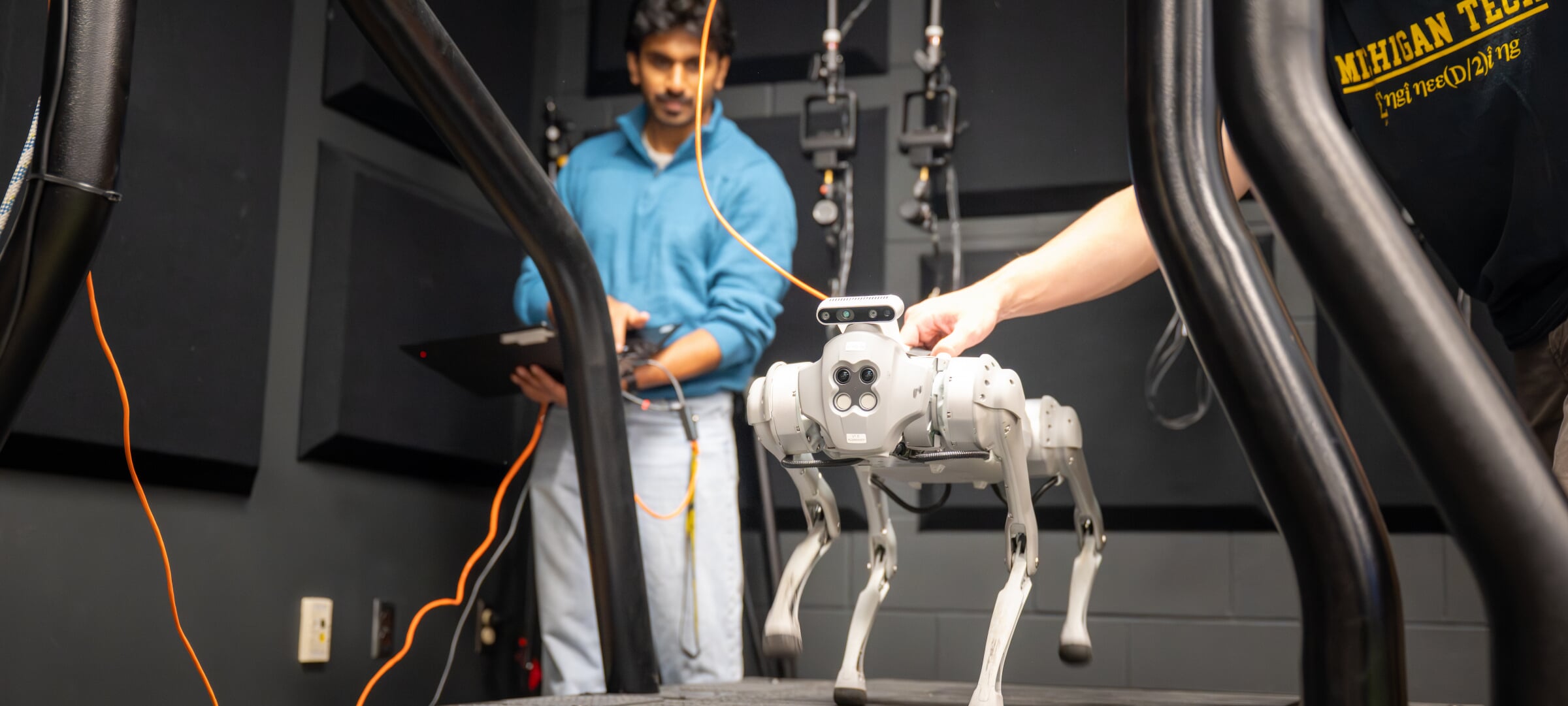 Two students monitor a dog robot walking on a treadmill.