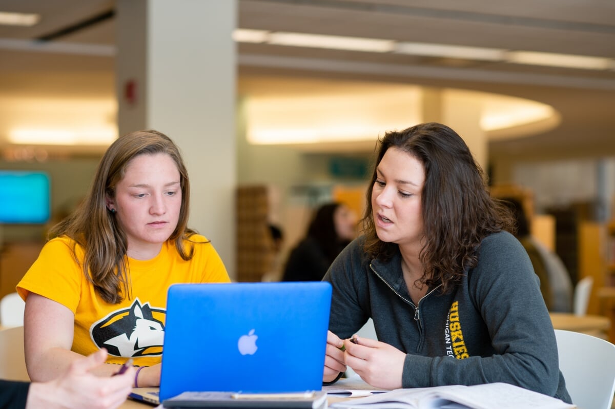 Two Michigan Tech graduate students working in front of their laptops while in a library.