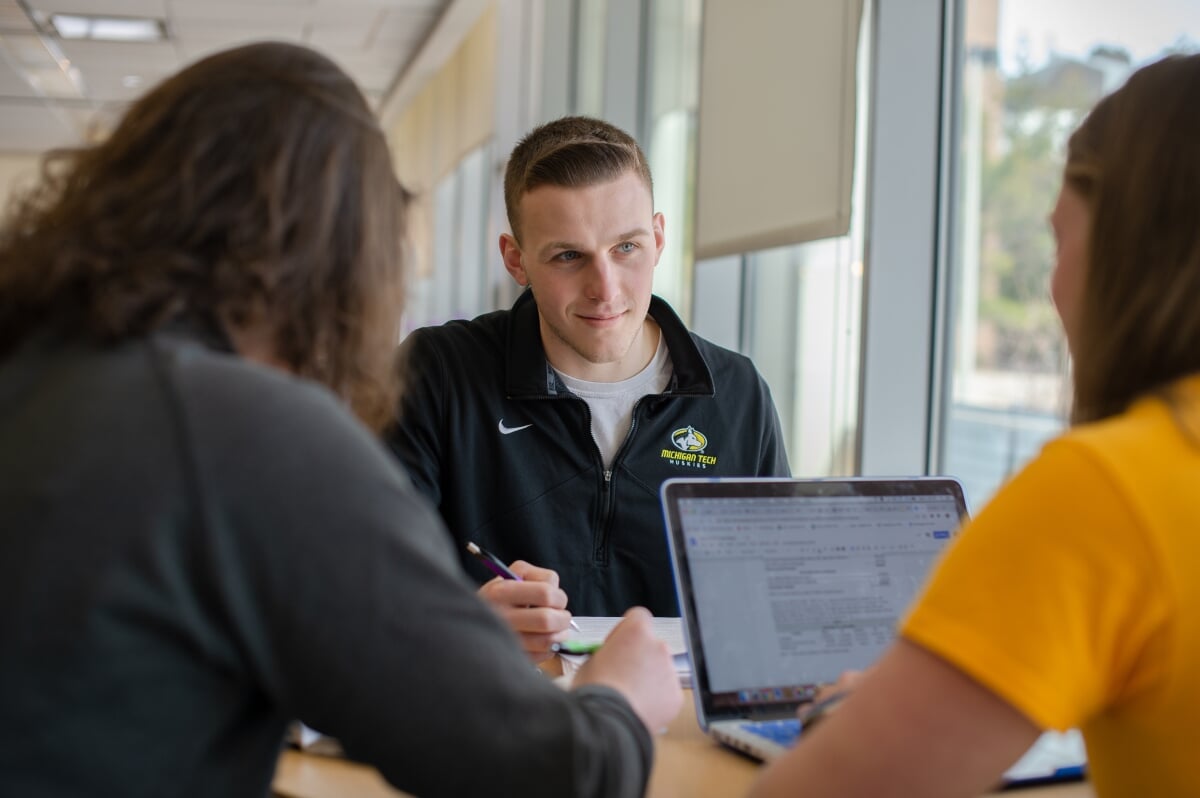 Three Michigan Tech students working in a library. They sit at a table with a laptop.