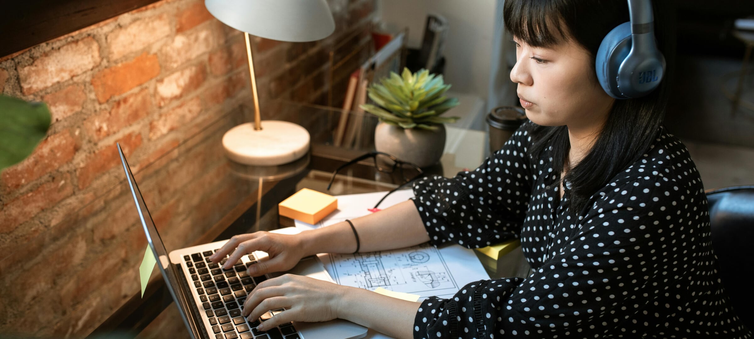 Female Asian student typing at computer while her arms rest on a plan/diagram.