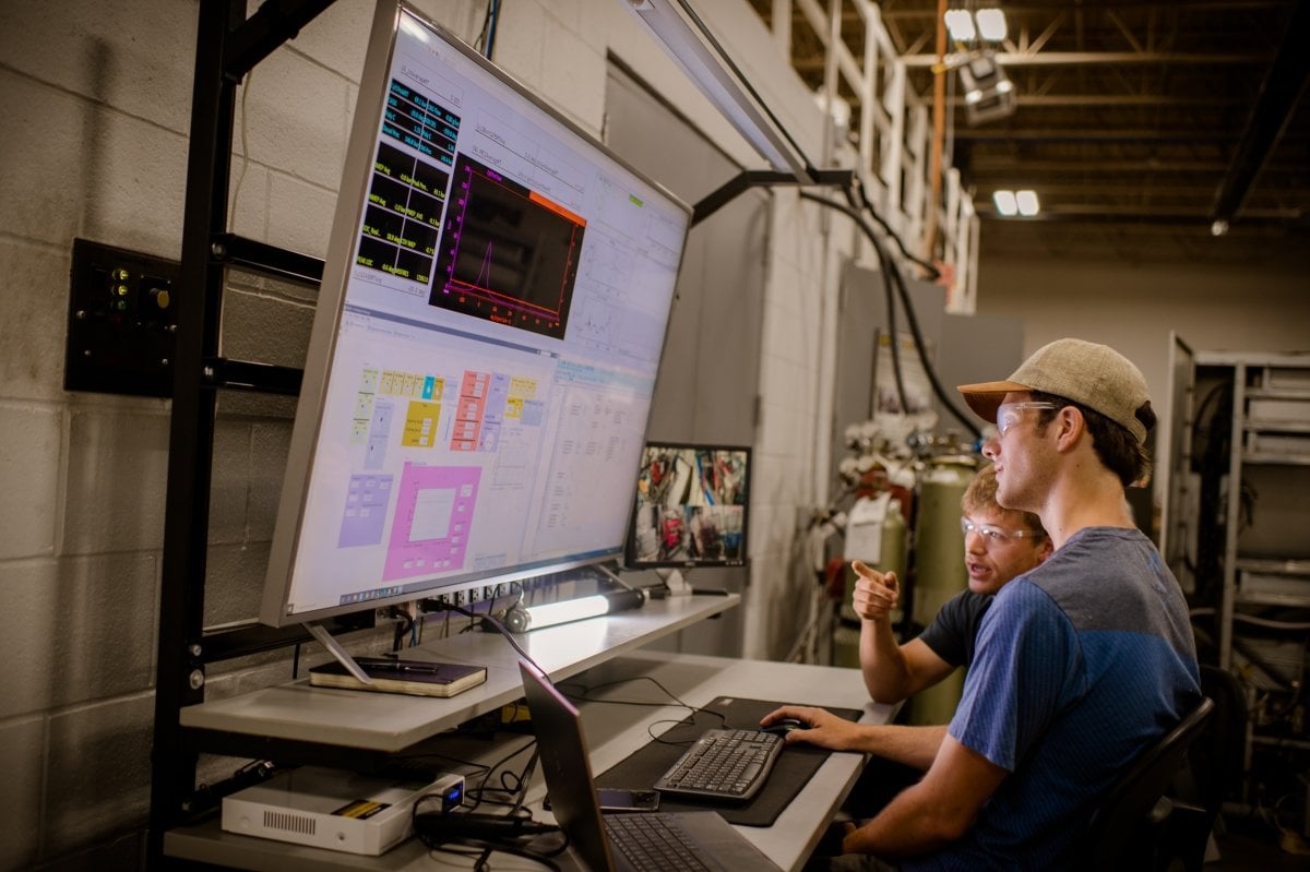 Two young men looking at two monitors as they discuss an instrrumemtation experiment