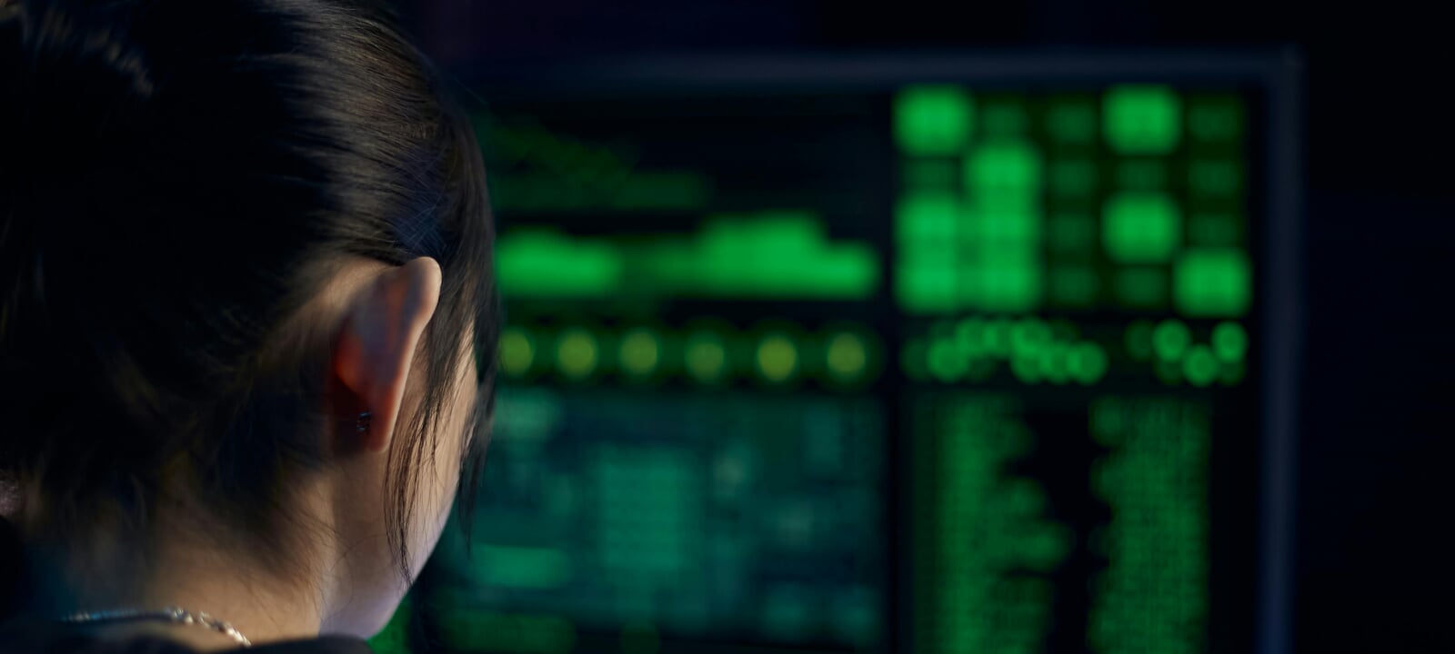 Woman looking at a bright green data visualization on a laptop screen in front of her.