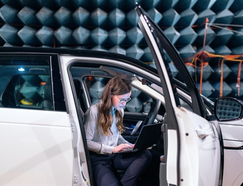 Female engineer with a laptop sits inside a vehicle while in an automotive testing center.