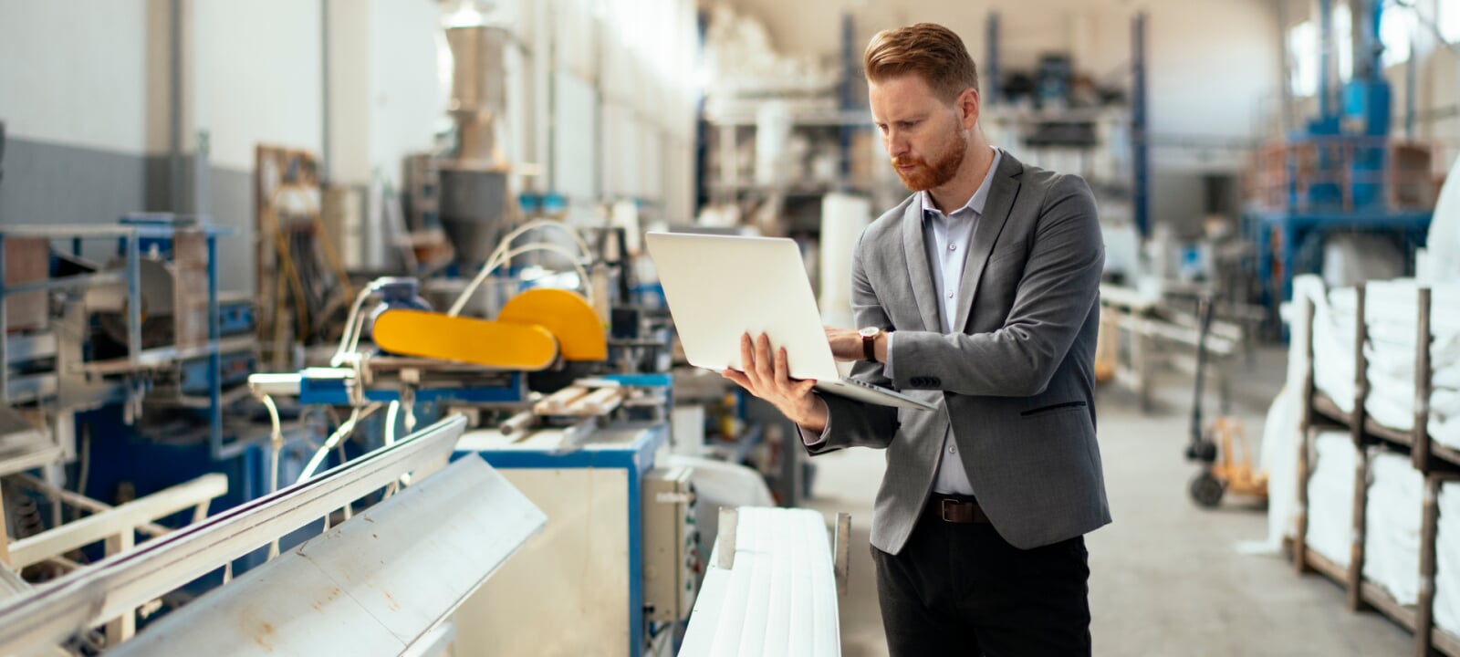 Business administration guy looking at a laptop while in an industrial engineering setting.