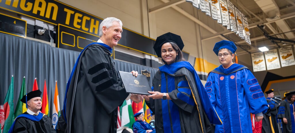 Graduate Student getting hooded by her advisor and the dean for her degree