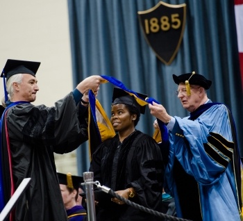    Graduate Student getting hooded by her advisor and the dean for her degree in Forest Science