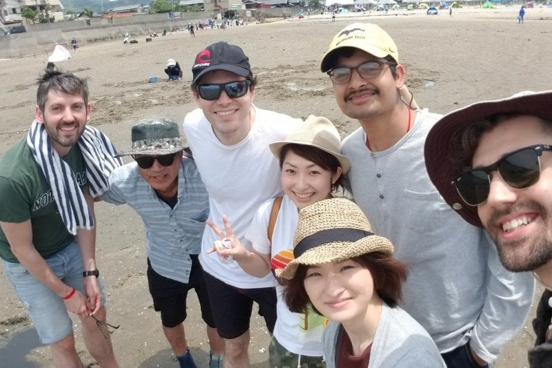 Adam and Shivom with cohorts digging clams at a beach in Japan