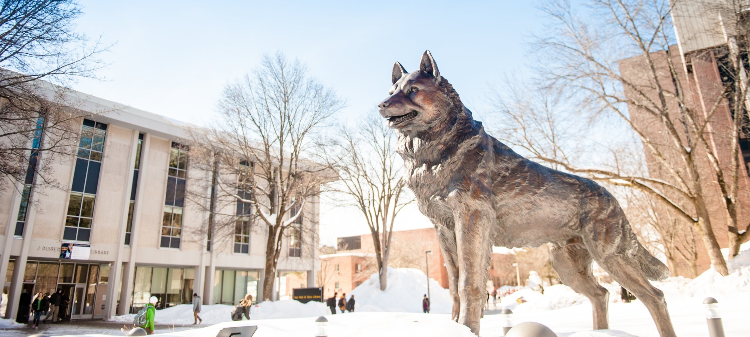 Students walk across campus in the snow. Husky statue in the winter.