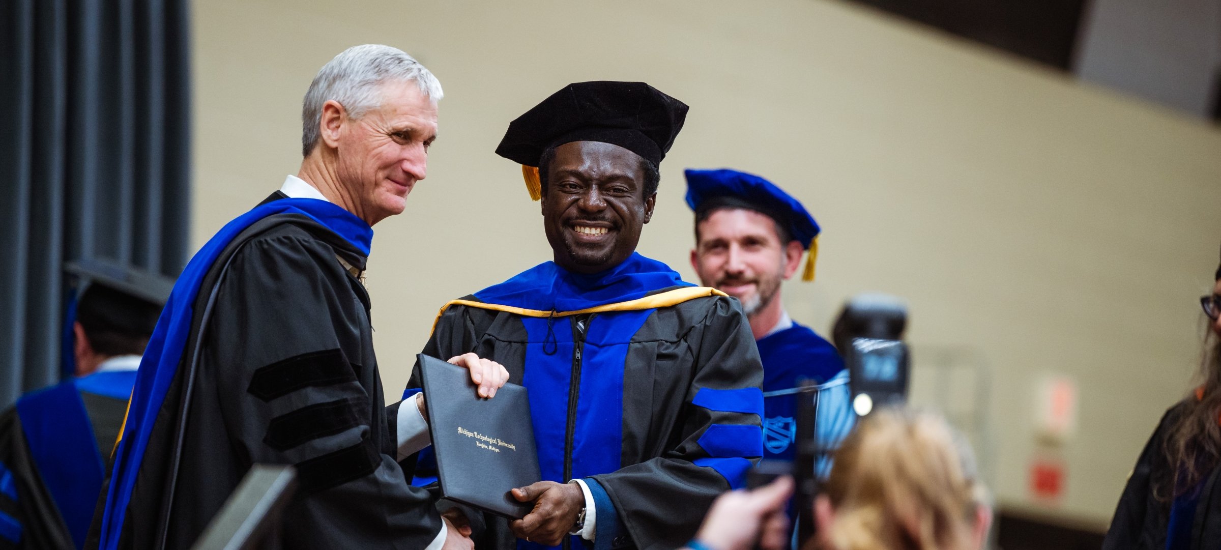 President Koubek and graduate student holding degree smiling for the camera.
